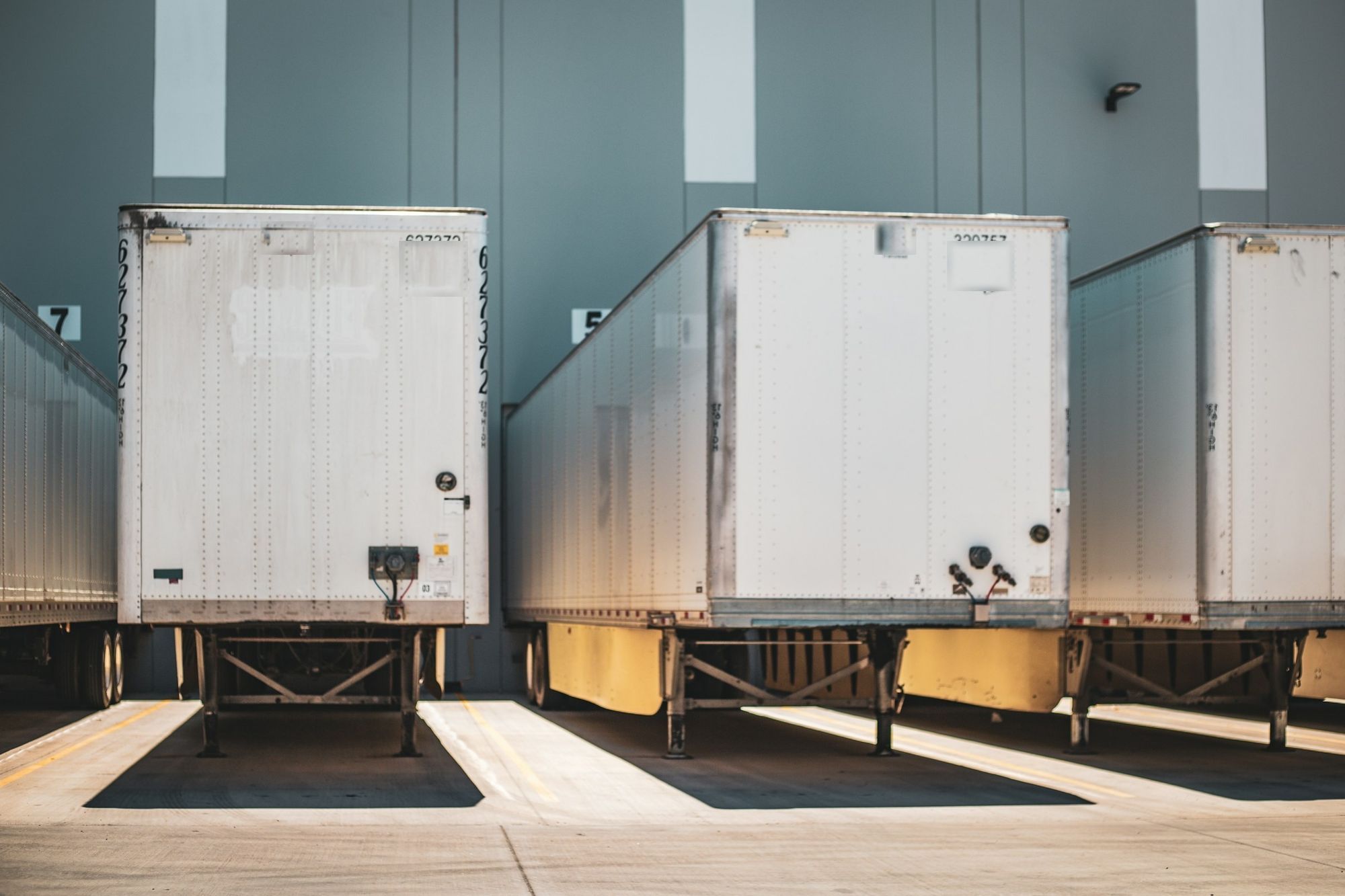 Three dry van trailers backed into loading dock doors at a warehouse.