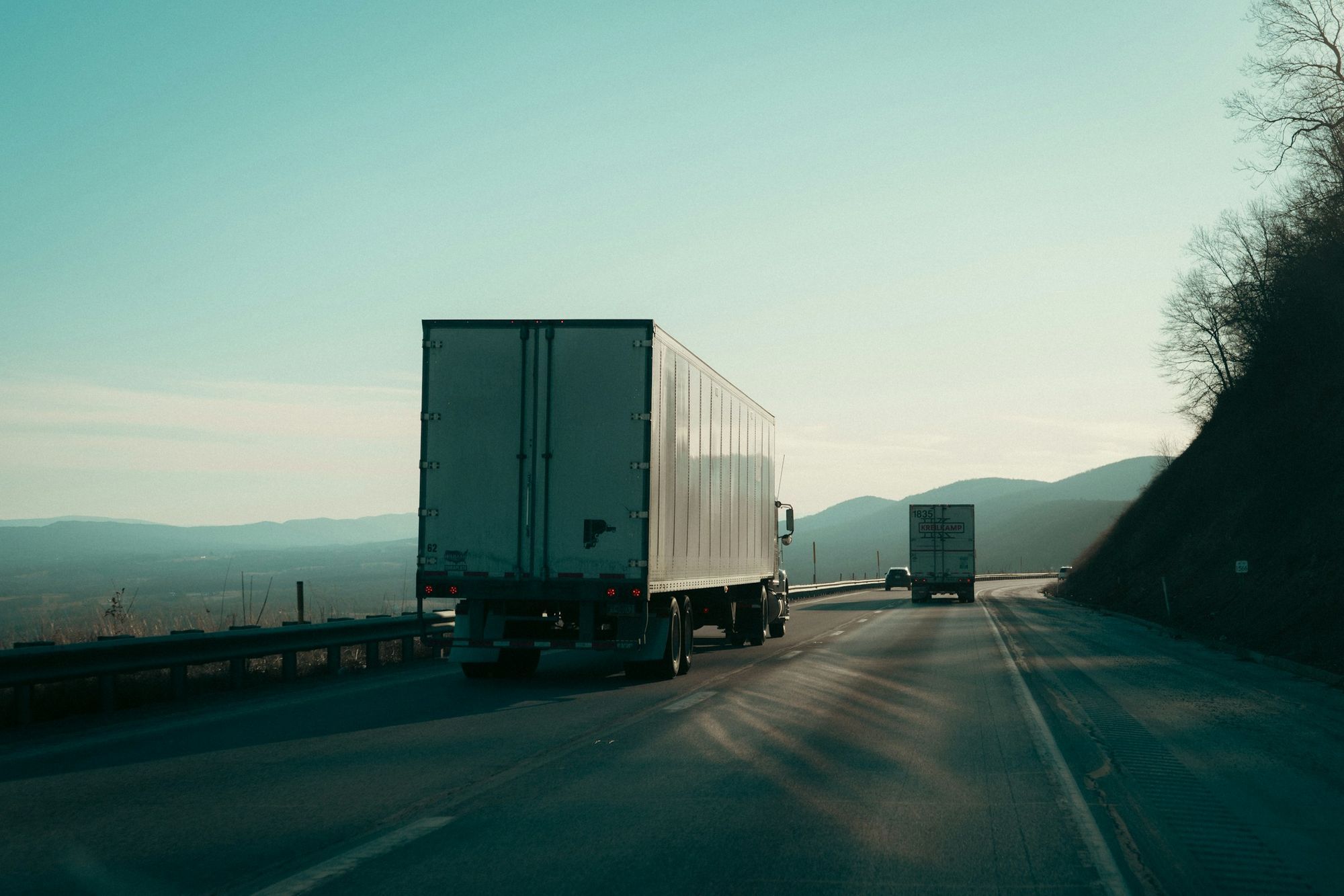 Rear view of a 53-foot dry van trailer on a mountain highway, a second truck ahead.