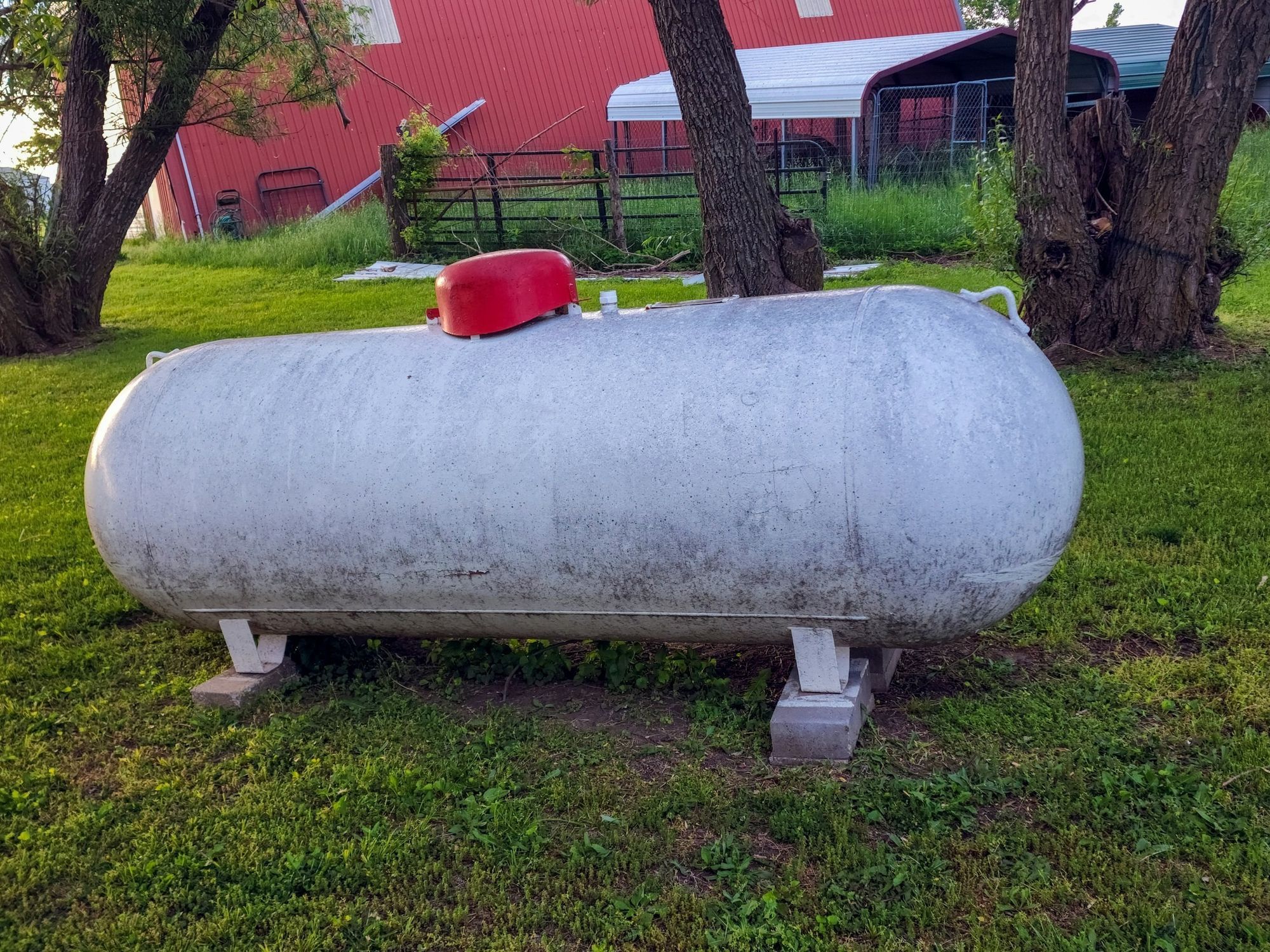 An empty horizontal ASME propane tank resting on concrete blocks on a farm.
