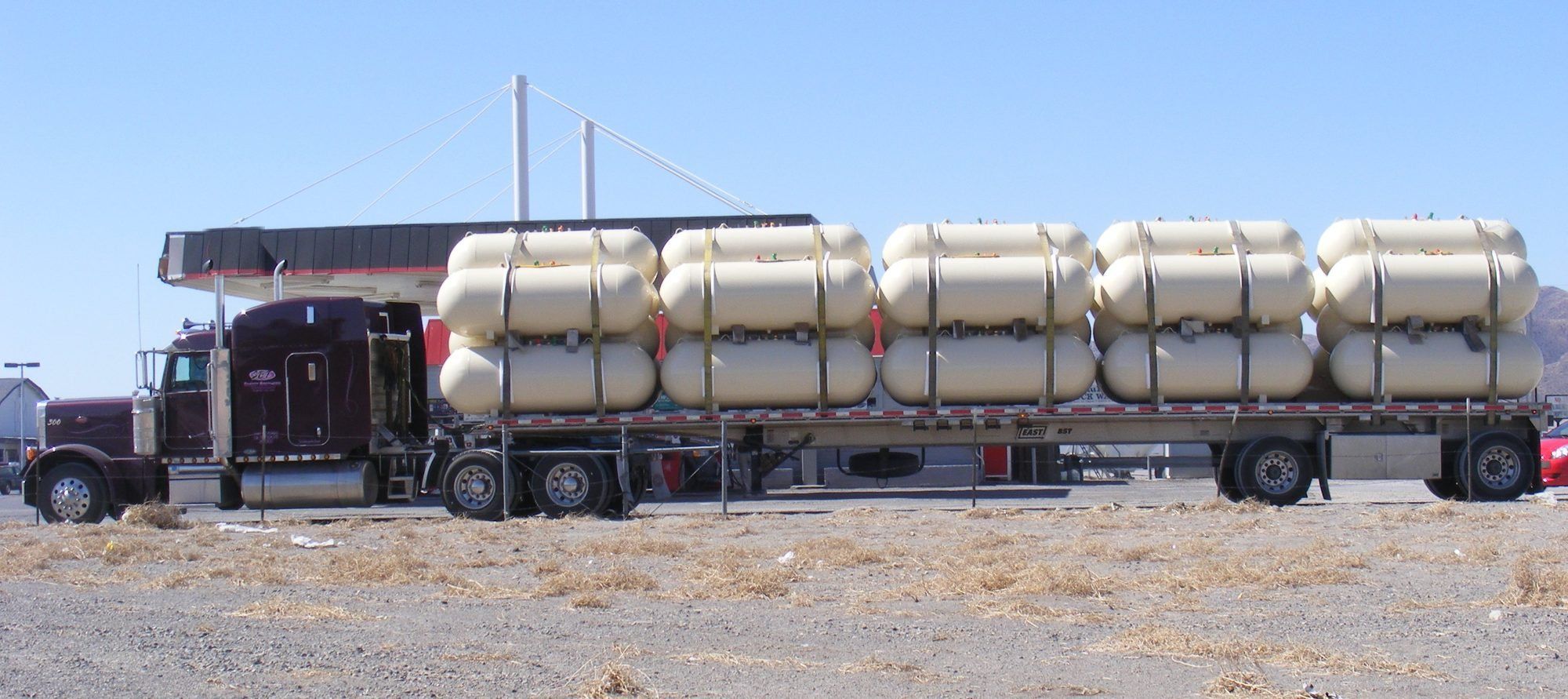 A conventional semi-truck pulling a flatbed loaded with fifteen empty ASME propane tanks, strapped in five stacks.
